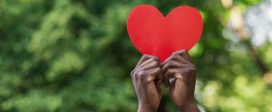 Black hands holding red paper heart on green background