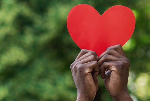 Black hands holding red paper heart on green background