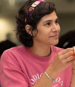 A young woman with dark hair gives a slight smile. she is wearing a pink top.